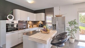 Eine moderne Küche mit weißen Schränken, einem Backofen von Bosch, einem Kühlschrank und einer Holztheke mit einer Obstschale.