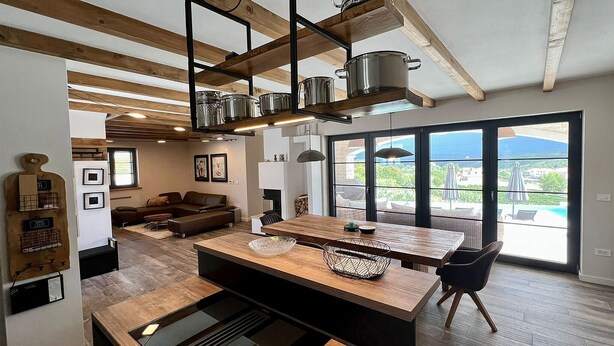 A modern kitchen with a central island, wooden beams, and large windows offering a view of the outdoors. - Stunning home in Vizinada (Vizinada)