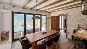 A spacious dining area with a wooden table and chairs, large windows with a view of a pool, and a stone wall. - Stunning home in Vizinada (Vizinada)