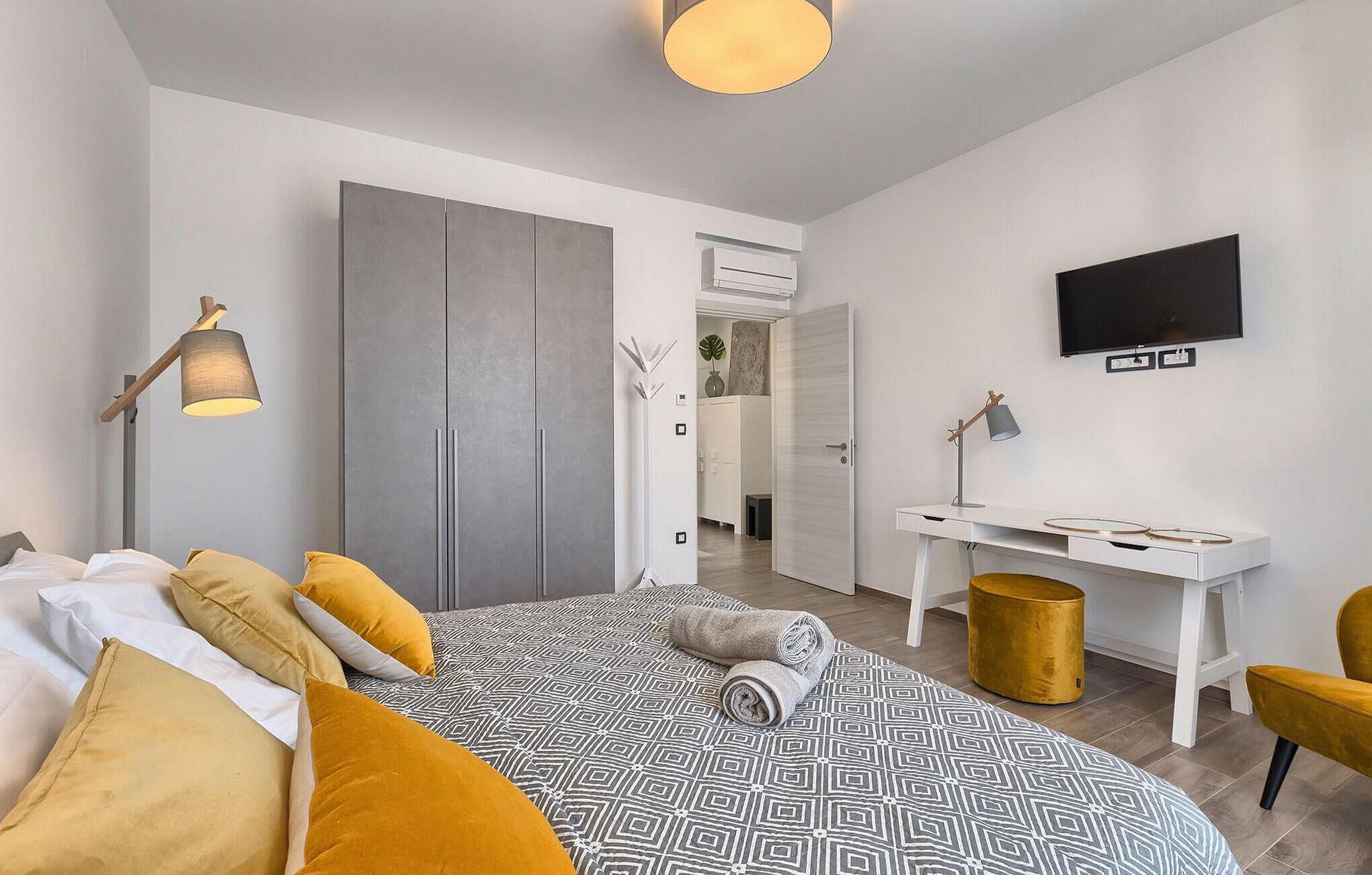 Een moderne slaapkamer met een bed, nachtlampje, bureau, stoel en een televisie.