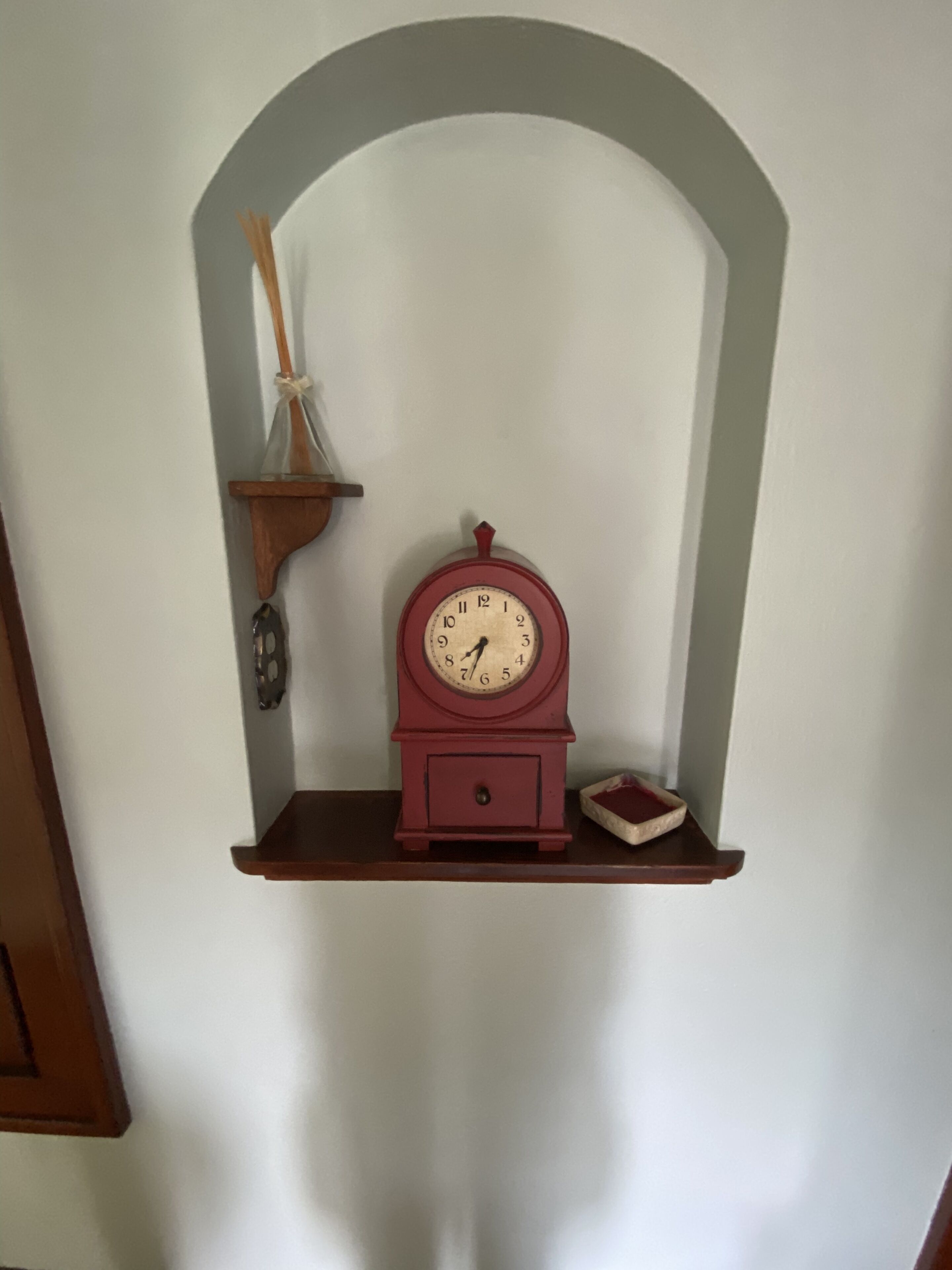 A wall-mounted shelf with a wooden clock, a small decorative item, and a glass container.