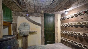 Una habitación rústica con pared de piedra, puerta de madera y varios contenedores de piedra en la pared.