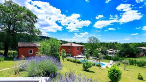 Una casa roja con techo de tejas, piscina y jardín con plantas de lavanda.