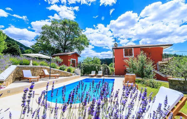 Un espace piscine avec un bâtiment rouge, deux chaises longues et un mur en pierre.