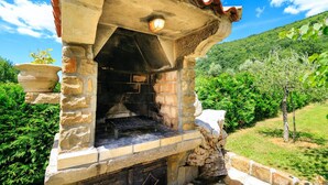 Un horno de piedra al aire libre con banco, rodeado de follaje y una ladera.