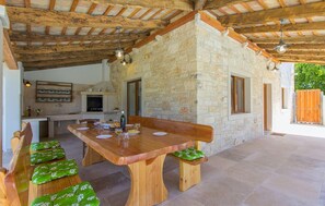 Un espace de restauration extérieur rustique, agrémenté d’un mur en pierre, de poutres en bois et d’une longue table en bois avec des bancs.
