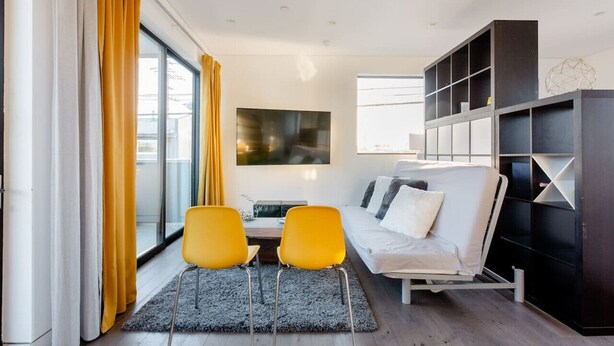 A modern living room with a sofa, two yellow chairs, a coffee table, and a TV mounted on the wall. - Cozy Luxurious 1 bed Loft style in Venice Beach (Los Angeles)