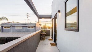 A modern balcony with a concrete floor, a wooden table and chairs, and a view of a neighboring building. - Cozy Luxurious 1 bed Loft style in Venice Beach (Los Angeles)