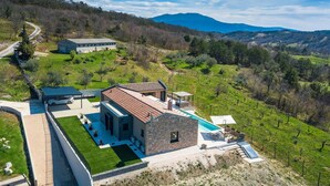 Une villa moderne dotée d’une piscine, d’une façade en pierre et offrant une vue sur les collines et les montagnes environnantes.