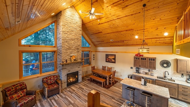 A spacious living area with a stone fireplace, wooden ceiling, and large windows offering a view of the outdoors. - Lake Views | Hot Tub | Games | Golf | Kayaks | St. Croix Casino (Turtle Lake)
