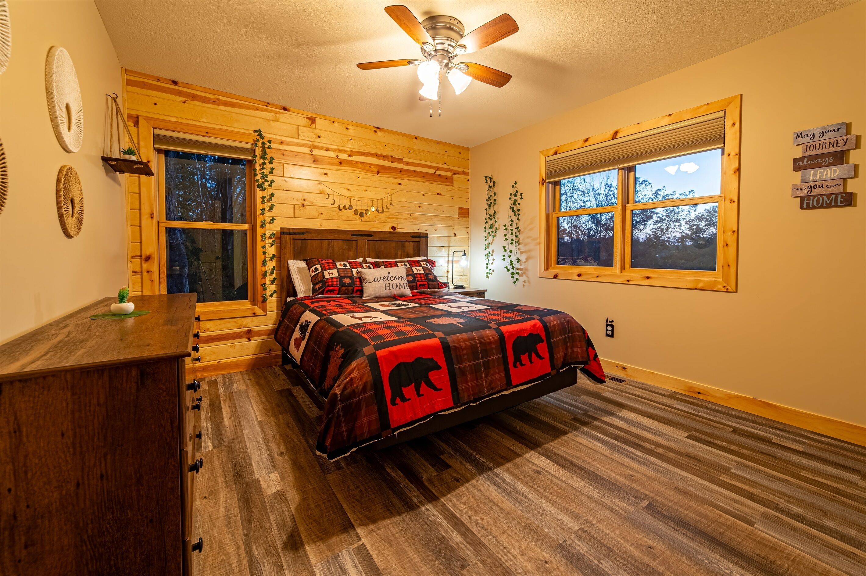 Une chambre confortable avec une tête de lit en bois, une grande fenêtre et un ventilateur de plafond.