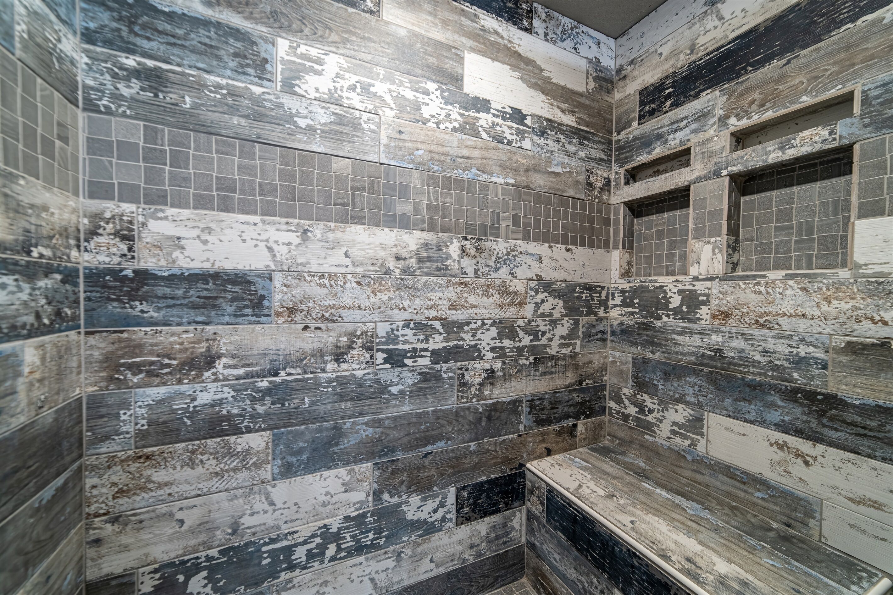 A bathroom with a rustic, distressed tile design and a built-in bench.