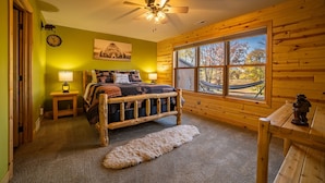 A cozy room with a wooden bed, a ceiling fan, a large window with a view, and a small table with a statue. - Lake Views | Hot Tub | Games | Golf | Kayaks | St. Croix Casino (Turtle Lake)