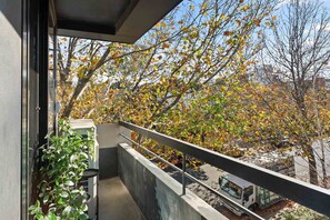 Een balkon met uitzicht op bomen met herfstbladeren, een betonnen balustrade en een gebouw op de achtergrond.