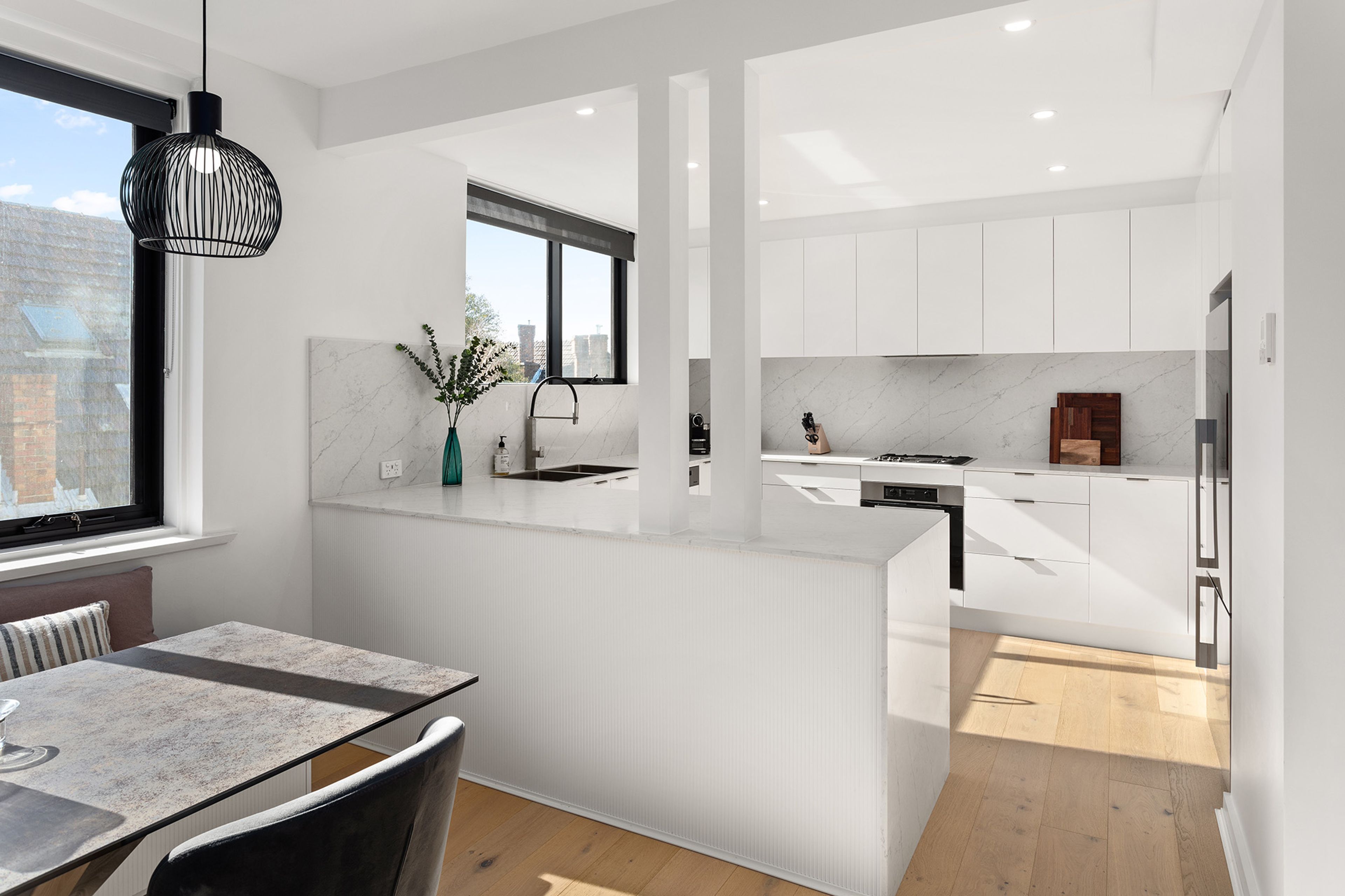 Una cocina moderna con armarios blancos, encimera de mármol y un comedor con mesa y sillas.