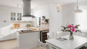 A modern kitchen with white cabinetry, a central island, and a dining area with a white table and chairs. - Cozy home in Labin - Rabac (Labin - Rabac)