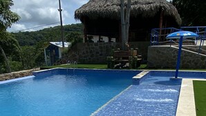 A swimming pool with clear blue water, a stone wall, and a thatched-roof structure in the background. - Ecohotel La Reserva (Piojó)