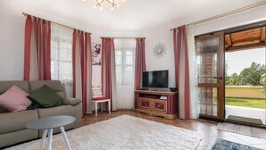 A living room with a sofa, a TV on a wooden cabinet, a small table, and a large window with curtains. - Gorgeous home in Porec (Porec)