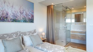 A bedroom with a bed, a nightstand, a glass shower enclosure, and a bathroom with a mirror and shelves. - Beautiful home in Pula (Pula)