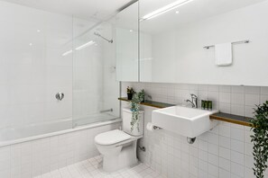 A modern bathroom with a glass shower enclosure, a toilet, a sink with a mirror above, and a small plant on the sink. - Watervue  in Docklands with City Views (Docklands)