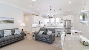 A modern living room with a grey sofa, a dining table, and a kitchen in the background.