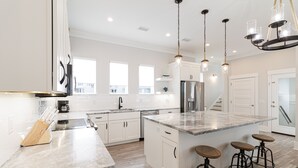 A modern kitchen with white cabinetry, a large island with stools, stainless steel appliances, and pendant lighting.