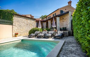 Ein Poolbereich mit Liegestühlen und Sonnenschirmen, Steinmauern und einem gepflegten Garten.
