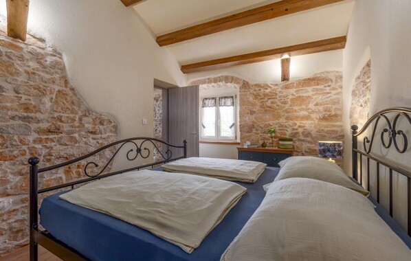 A bedroom with two beds, stone walls, wooden beams, a window with curtains, and a bedside table with a lamp. - Awesome home in Labin - Rabac (Labin - Rabac)