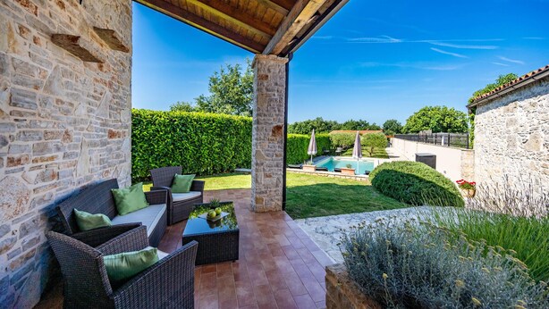 A covered patio with wicker furniture, a stone wall, and a view of a swimming pool. - Awesome home in Labin - Rabac (Labin - Rabac)
