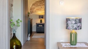 A hallway with a stone wall, a green vase with flowers, a lamp with a floral lampshade, and a small table with a lace doily. - Awesome home in Labin - Rabac (Labin - Rabac)