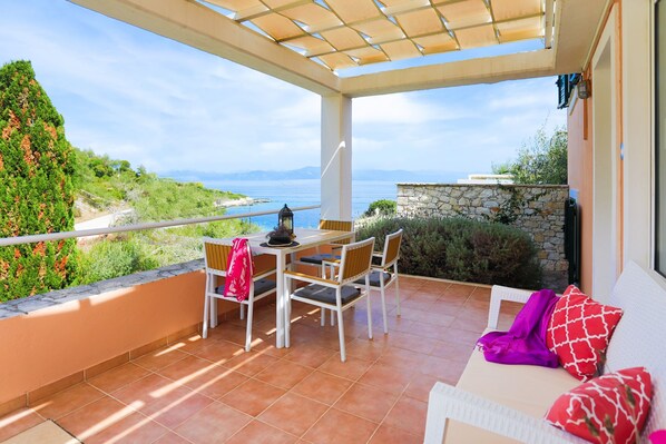 A balcony with a table and chairs, overlooking a scenic view of the sea and greenery.