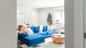 Un salon moderne avec un canapé bleu, une table basse ronde et une grande fenêtre équipée de stores.