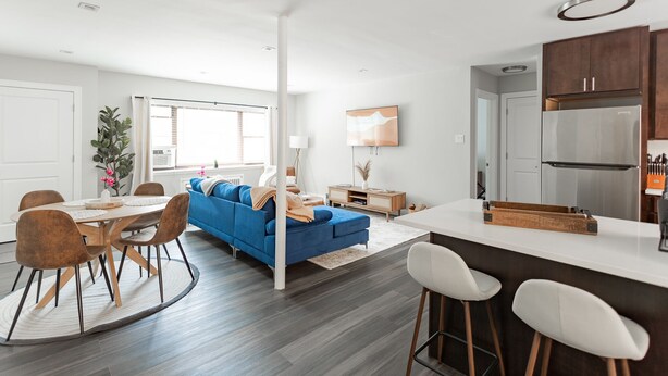 Un salon moderne avec un canapé bleu, un coin repas doté d’une table ronde et une cuisine équipée d’appareils électroménagers en acier inoxydable.