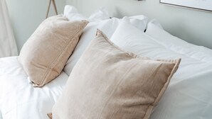 Un lit avec du linge de lit blanc et des oreillers de couleur beige.