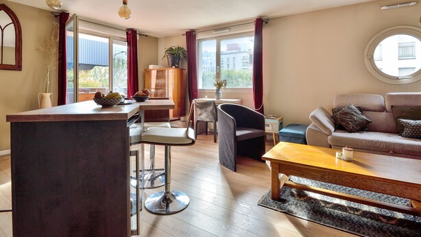 Ein modernes Wohnzimmer mit Holztisch, einer Couch, einem Essbereich mit Tisch und Stühlen sowie einem großen Fenster mit Vorhängen.