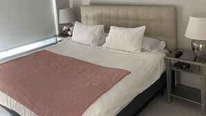 Ein modernes Hotelzimmer mit einem großen Bett, einem Nachttisch mit Lampe und Blick auf die Stadt durch das Fenster.