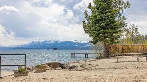 A beach with a wooden deck, picnic tables, and a view of snow-capped mountains.