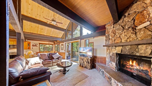 A spacious living room with a stone fireplace, leather sofas, and a large window overlooking a forested area.