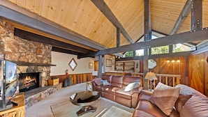 A cozy living room with a stone fireplace, leather sofa, and wooden beams.
