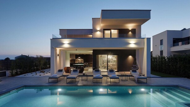 A modern two-story house with a swimming pool, outdoor seating, and a view of the surrounding landscape.