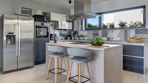 A modern kitchen with a stainless steel refrigerator, built-in oven, and a large island with bar stools.