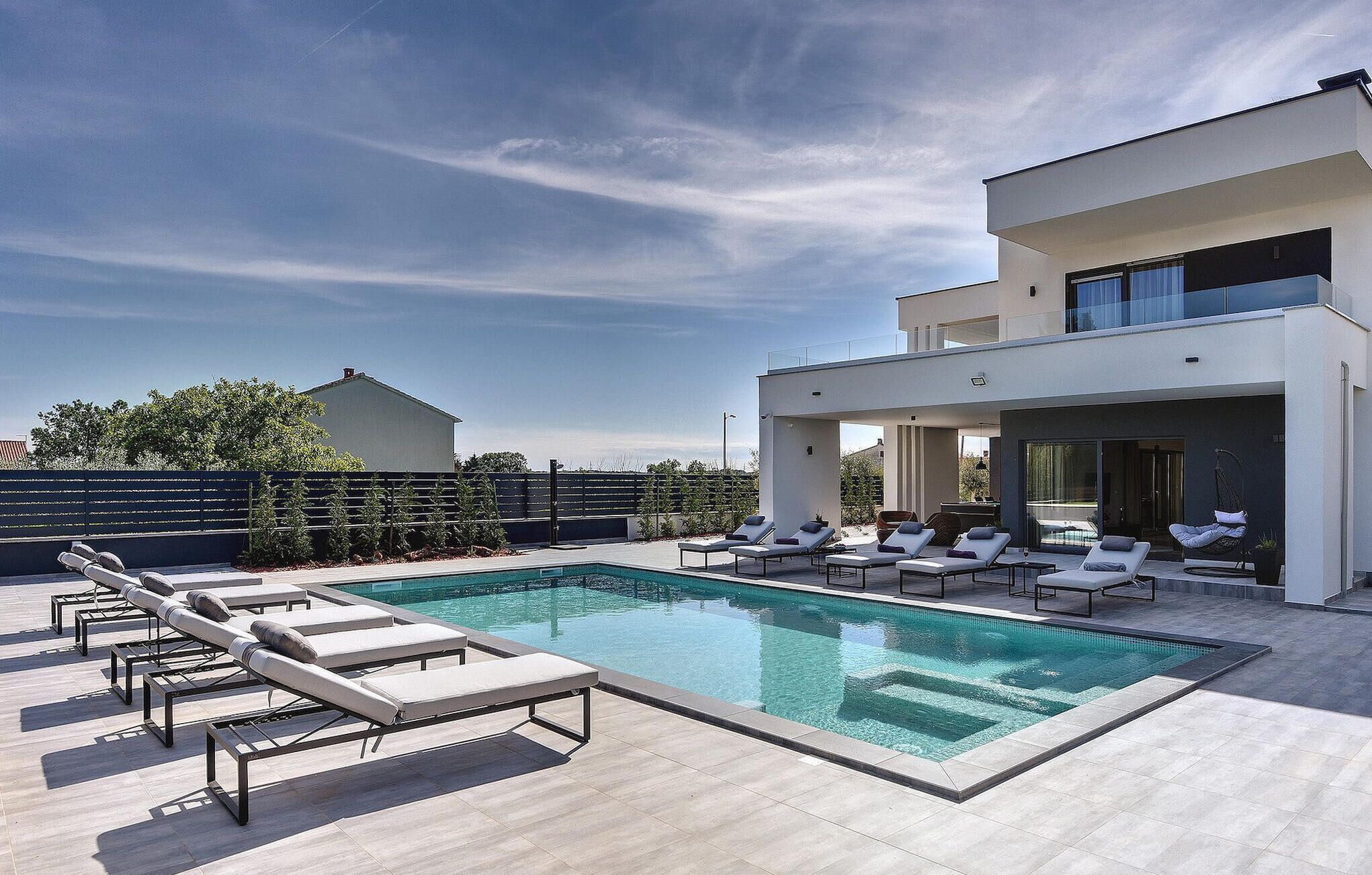 Un espace piscine extérieur moderne, doté de chaises longues et d’un bâtiment au design contemporain.