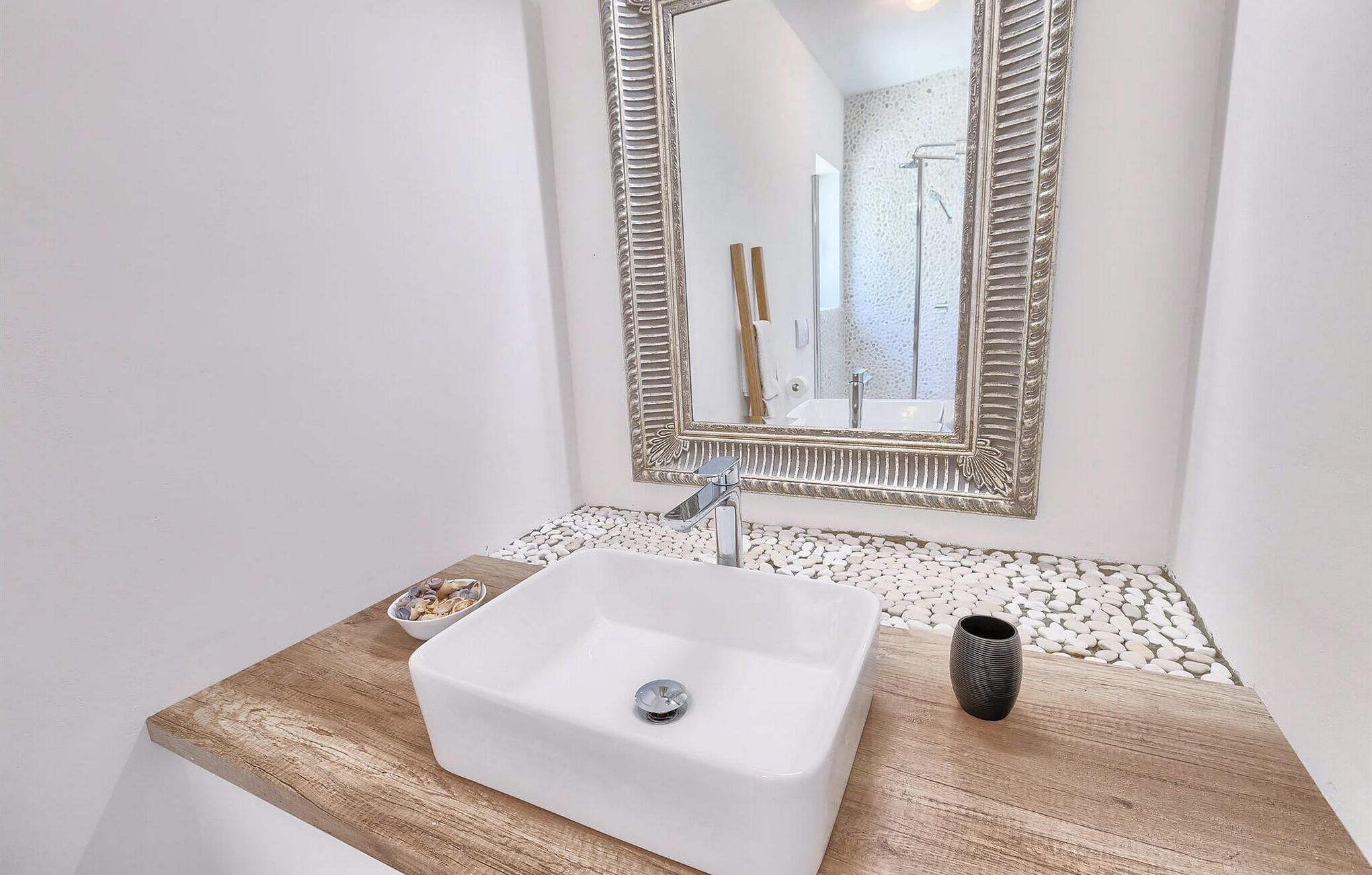 A bathroom with a white sink, a wooden countertop, and a mirror with a decorative frame.
