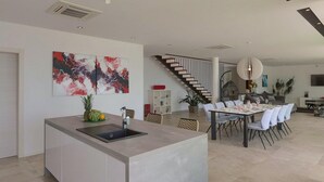 Une cuisine moderne avec un îlot central, un coin repas avec des chaises blanches, un escalier et des œuvres d’art abstraites accrochées au mur.