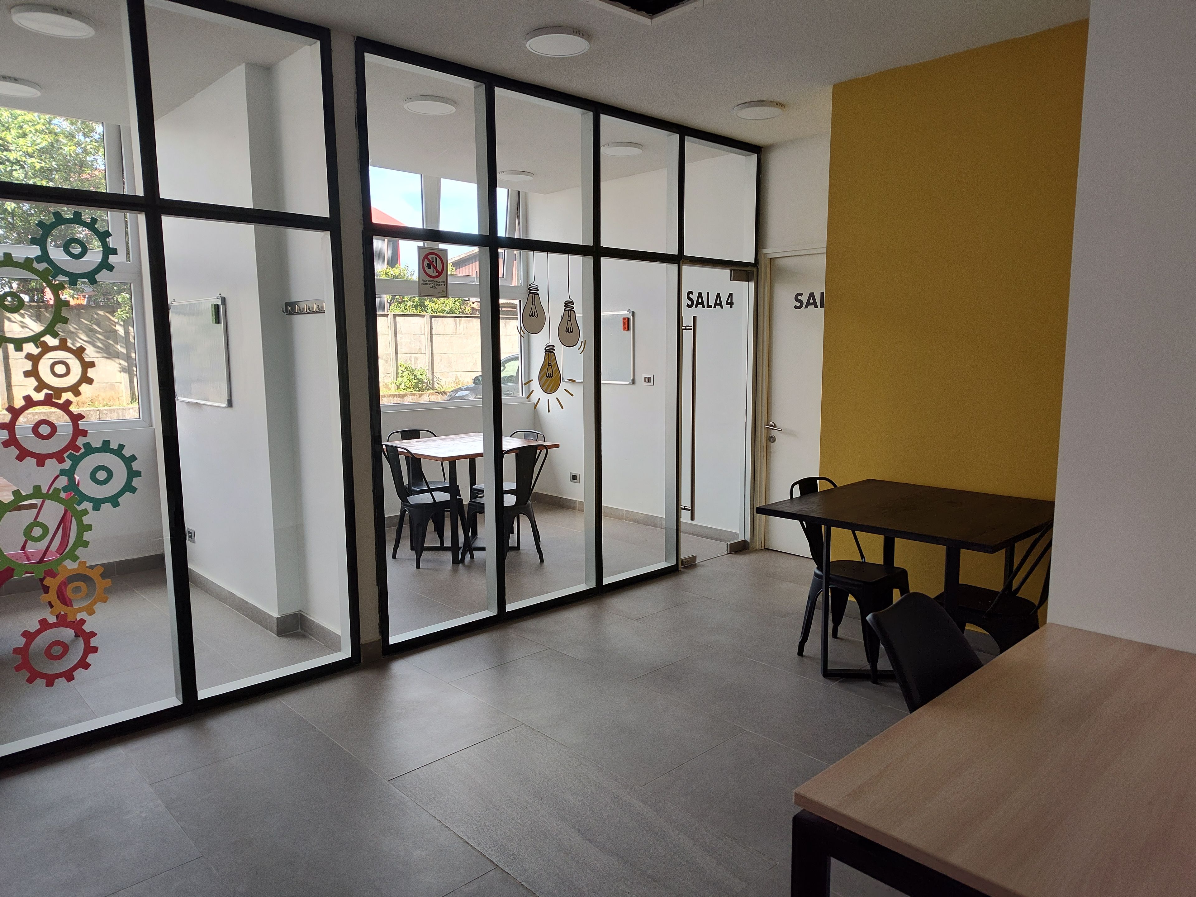 A modern interior with glass partitions, a dining area with chairs, and a yellow accent wall.