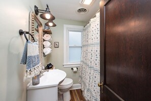 Ein Badezimmer mit weißem Waschbecken, Toilette, Spiegel mit Handtuchhalter und Duschvorhang.