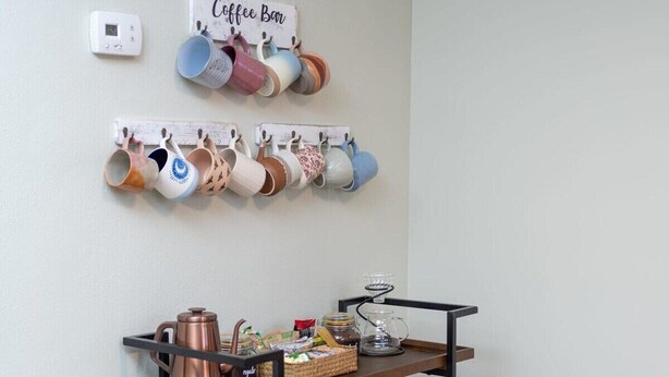 Disposición de una cafetería con tazas en un estante de pared, una máquina de café y una bandeja con utensilios para preparar café.