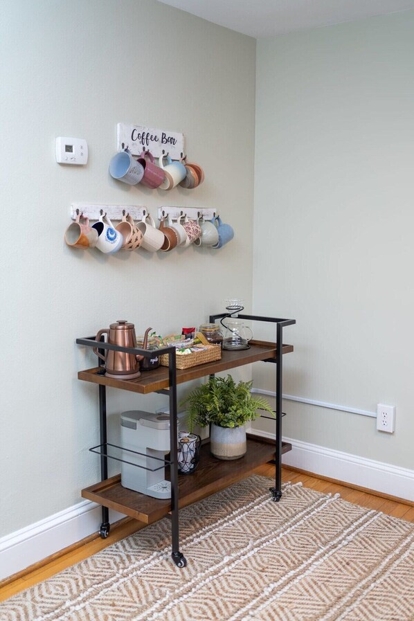 A coffee bar setup with mugs on a wall-mounted rack, a coffee machine, and a tray with coffee-making accessories.
