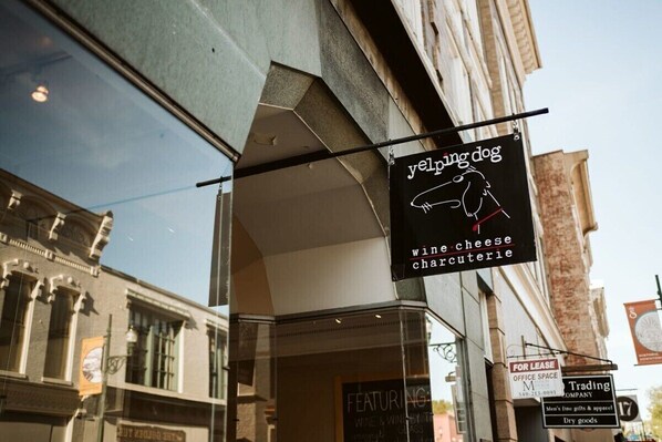Una tienda con un letrero que dice 'yeling dog', mostrando una tabla de quesos y fiambres acompañada de vino.