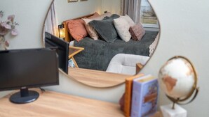 Un dormitorio con cama, escritorio, monitor de computadora, un globo terráqueo y un espejo que refleja la habitación.